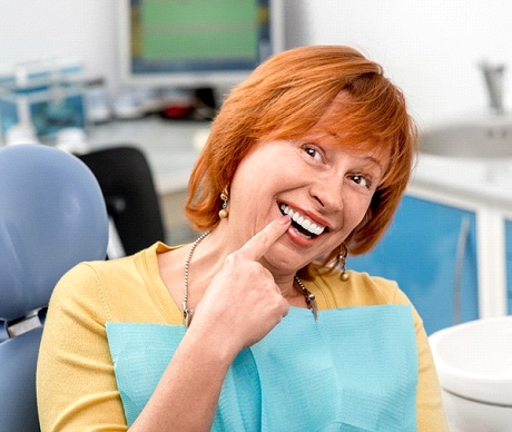 An older woman pointing to her smile