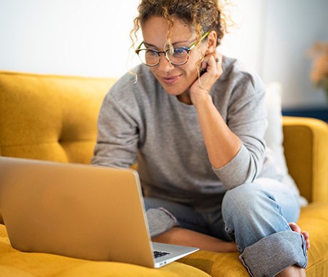 Woman with glasses smiling while looking at laptop