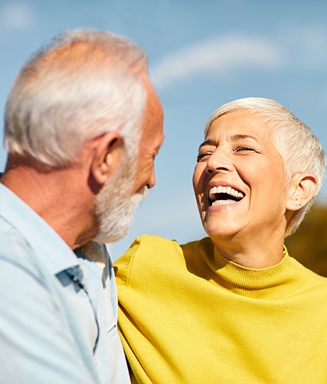 Senior woman in yellow shirt laughing while speaking to senior man