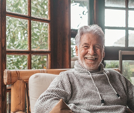Man in grey sweater smiling while sitting in cushioned wooden chair