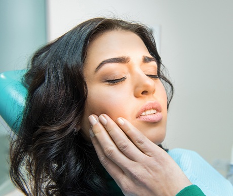 Woman in dental chair holding cheek