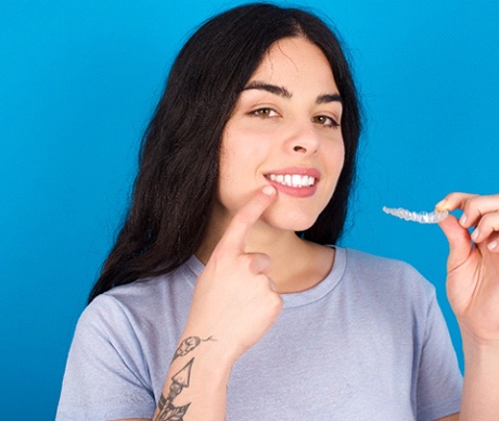 Woman holding SureSmile aligner, pointing at her teeth